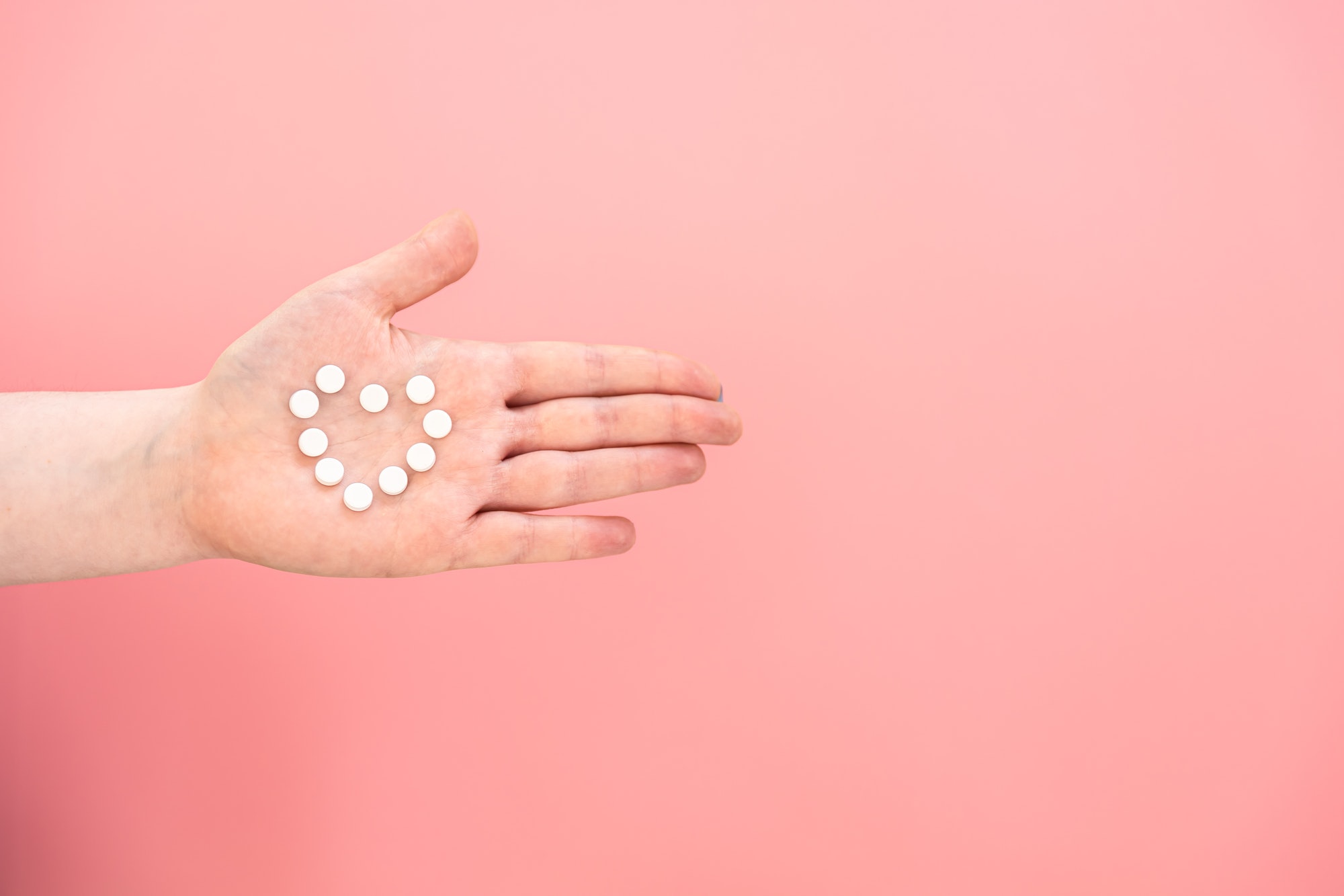 Pills in the shape of a heart on a female palm, pink background.